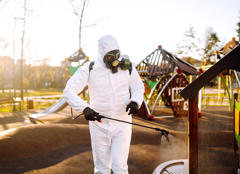 Man wearing protective suit disinfecting the playground in the sun with spray. Covid -19. Cleaning.