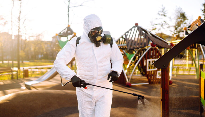 Man wearing protective suit disinfecting the playground in the sun with spray. Covid -19. Cleaning.